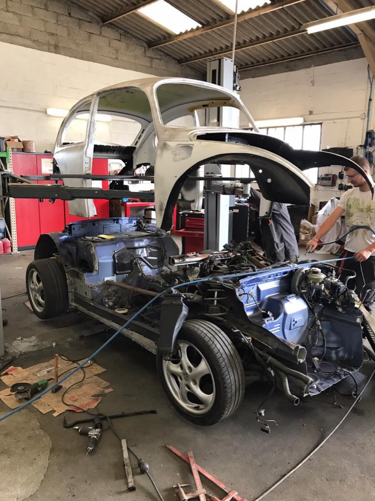 VW bug's body shell being lowered onto a 2001 Porsche Boxter frame chassis drivetrain